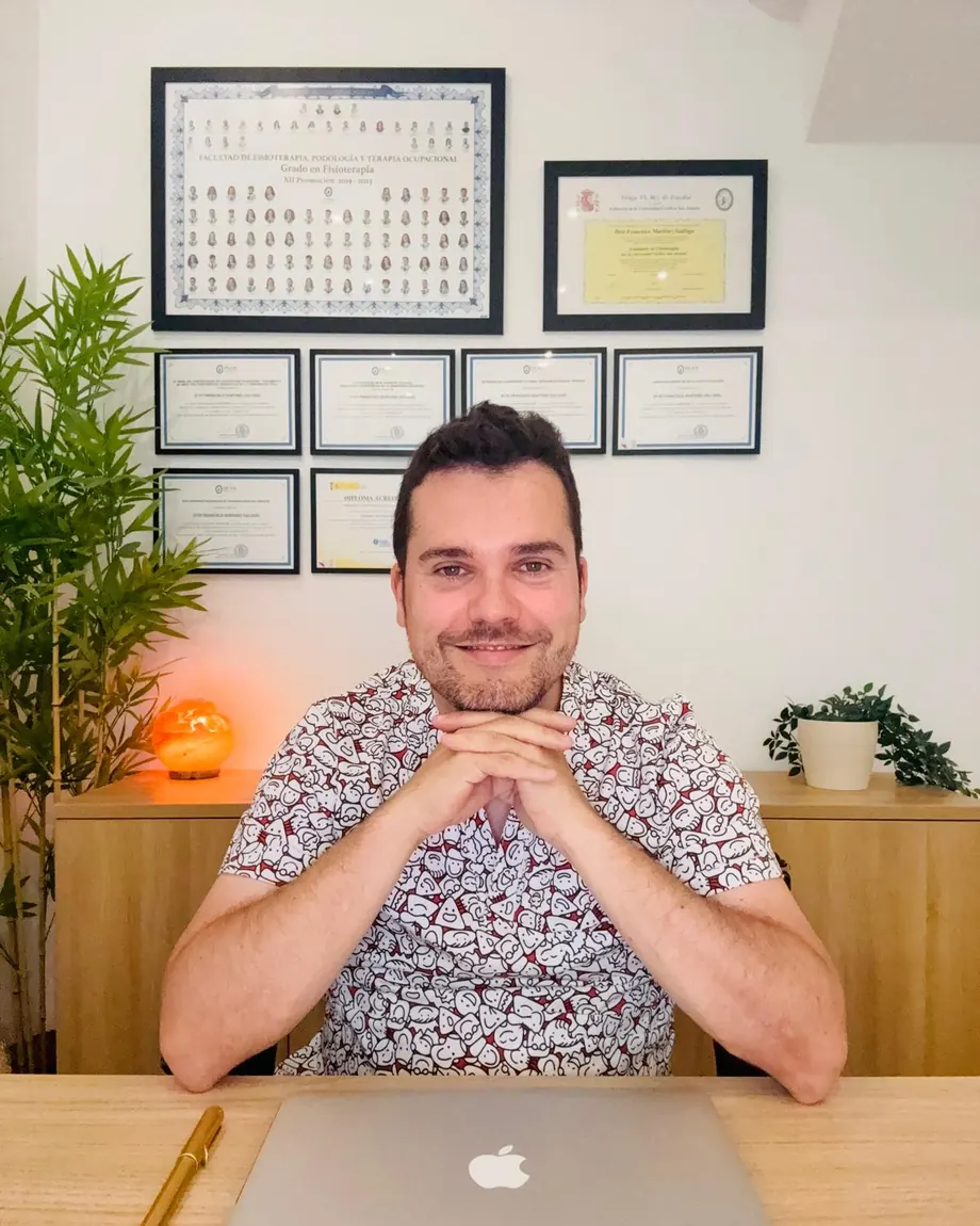 Fran Martínez, fisioterapeuta, sentado a la mesa de su consulta, con sus títulos en la pared