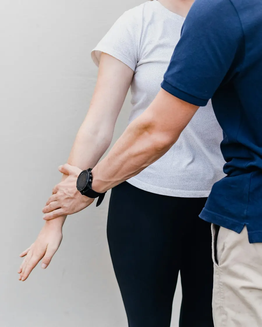Las manos de quien trata guían el brazo de una paciente de pie